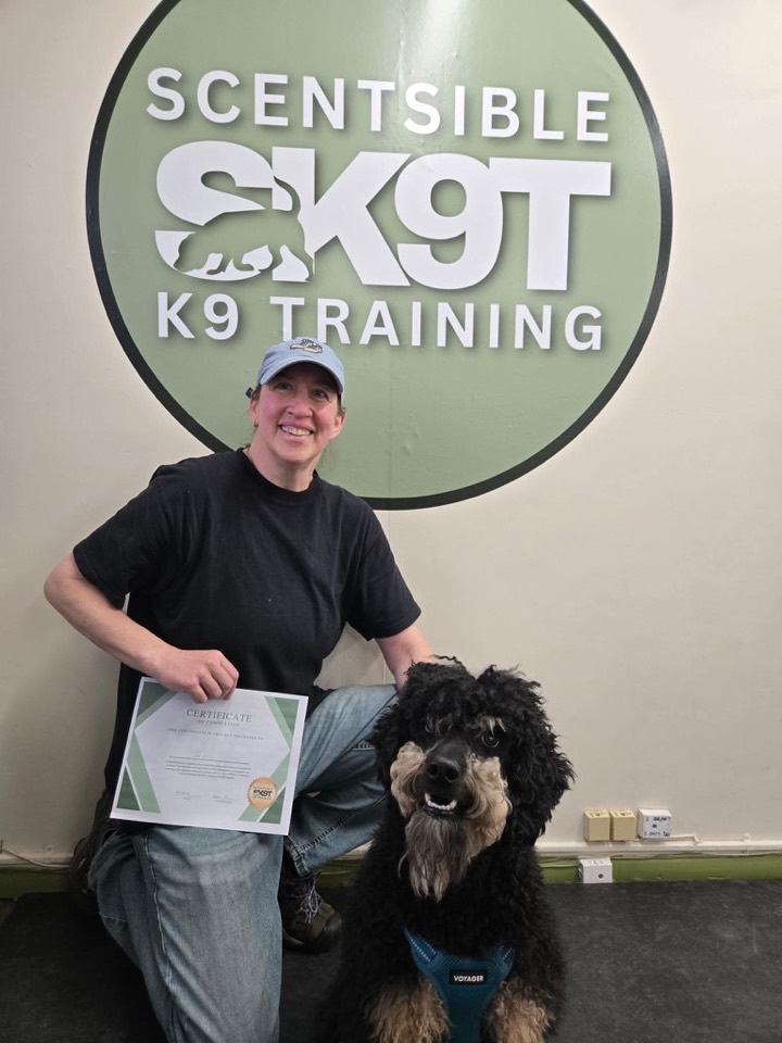 A client and their black doodle with a graduation certificate